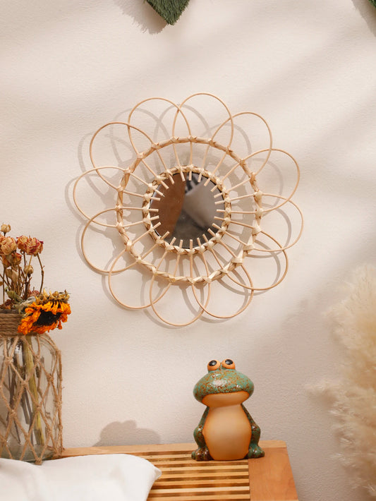 Handwoven round bamboo wall mirror with sun- and flower-inspired design mounted on a wall
