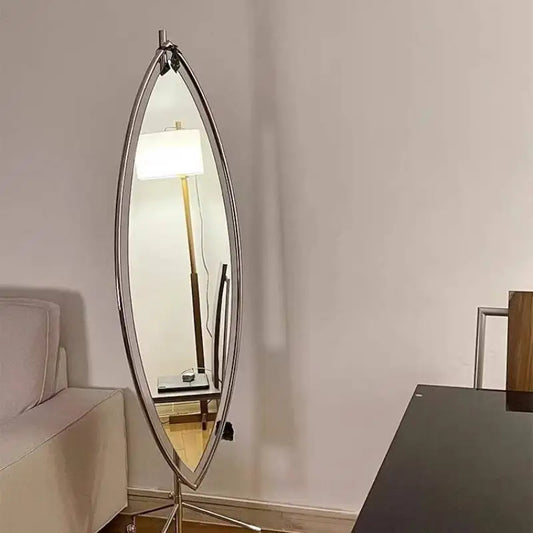 Modern oval full-length standing mirror with a slim metal frame, placed in a minimalist living room beside a sofa and floor lamp.