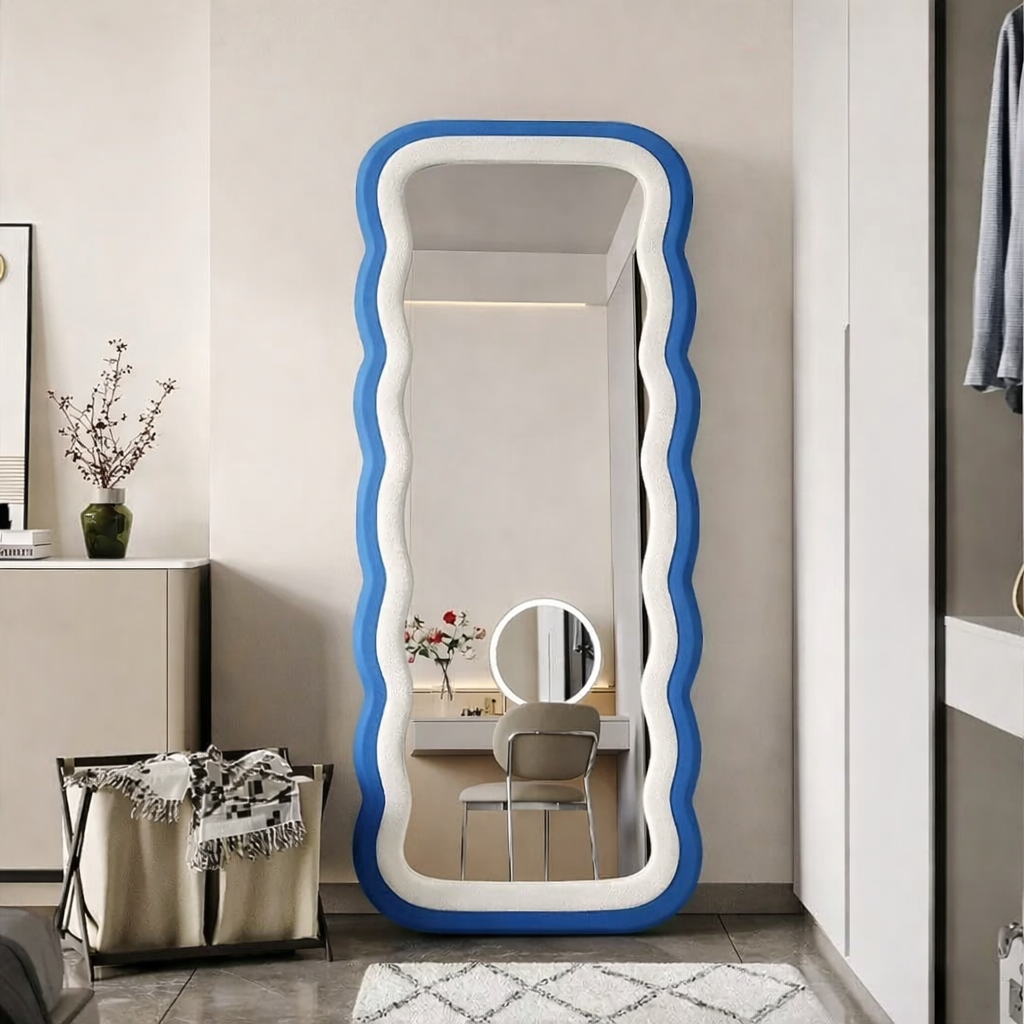 Modern full-length standing mirror with a wavy blue frame, styled in a contemporary bedroom with neutral decor.