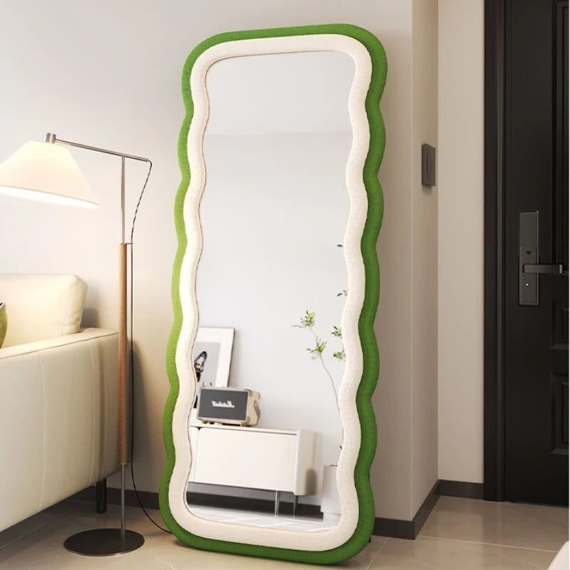 Modern full-length standing mirror with a wavy green frame, styled in a contemporary bedroom with neutral decor.