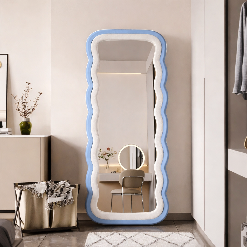 Modern full-length standing mirror with a wavy light blue frame, styled in a contemporary bedroom with neutral decor.