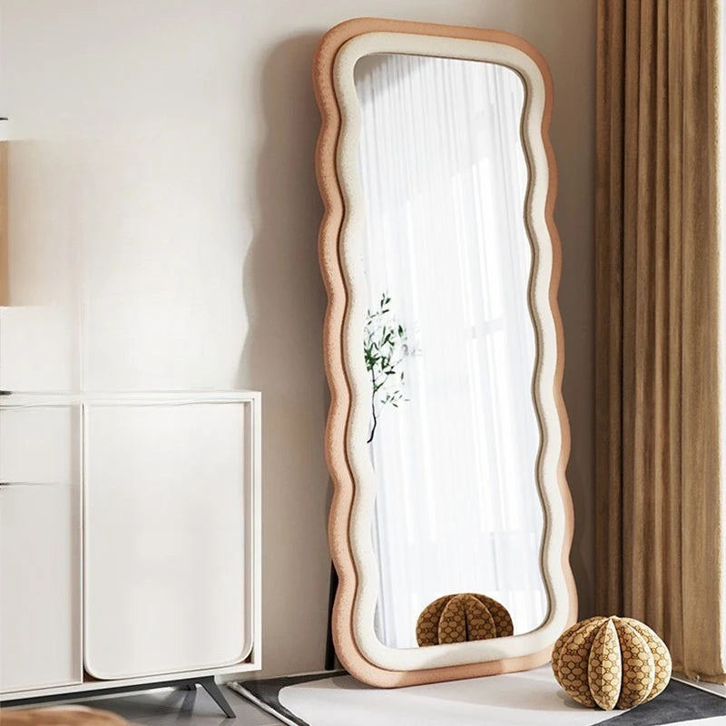 Modern full-length standing mirror with a wavy peach frame, styled in a contemporary bedroom with neutral decor.

