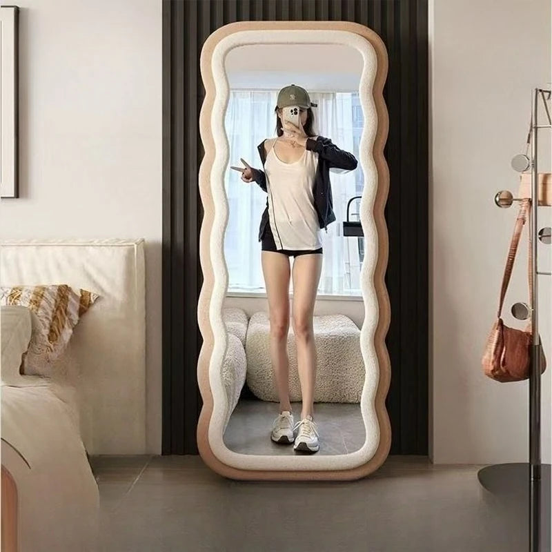 Modern full-length standing mirror with a wavy peach frame, styled in a contemporary bedroom with neutral decor.

