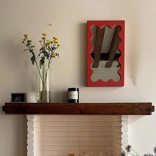 Red wavy wooden wall mirror with irregular scalloped frame mounted above a rustic fireplace mantel